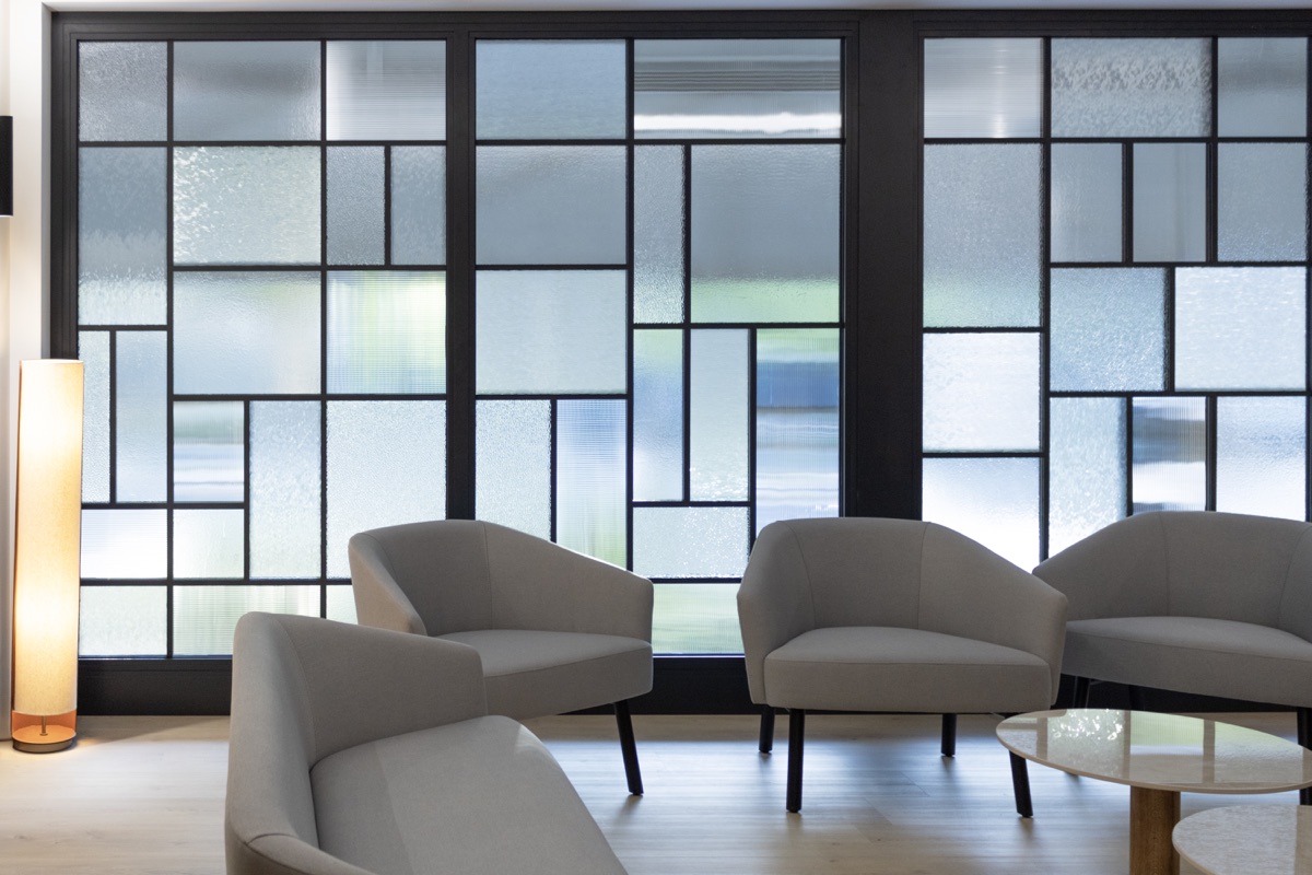 Verrière aux vitraux géométriques Art déco et fauteuils contemporains dans un salon des Salons Lecreux